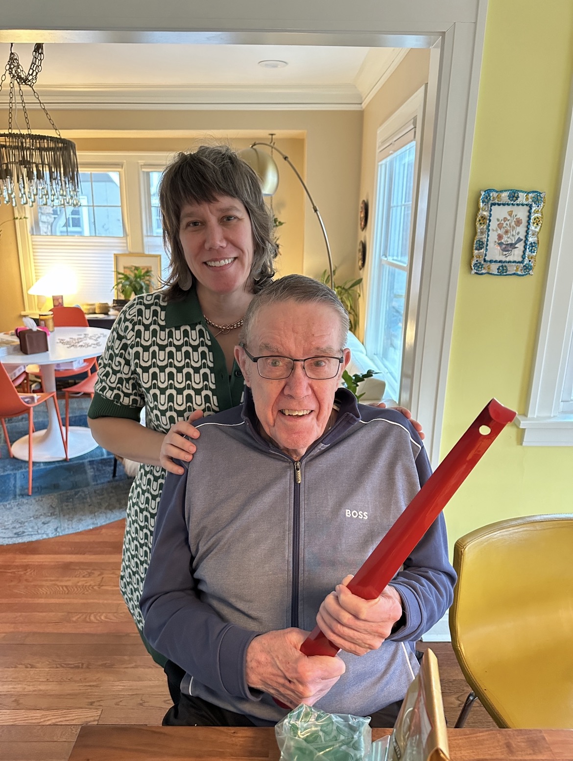 Mom standing behind Grandpa as he opens a gift